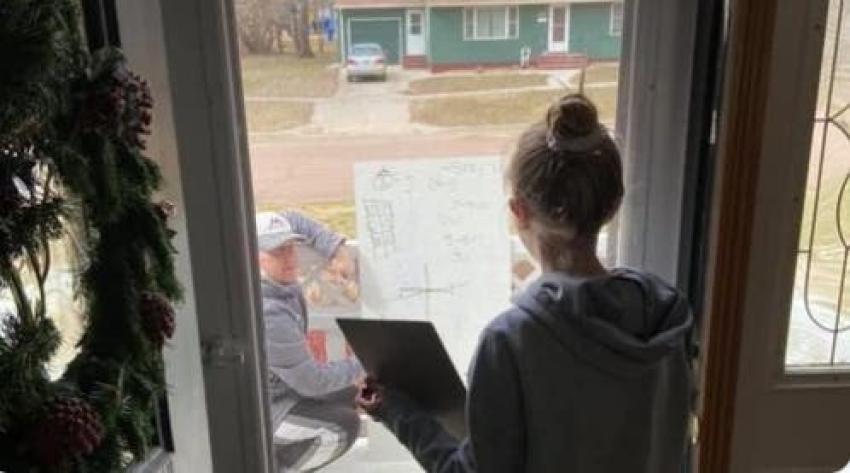 Profesor ayuda a estudiante con su tarea a través de la ventana de su casa en cuarentena